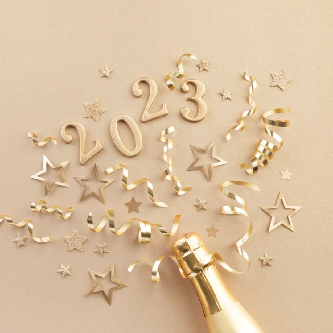 A festive celebration image with 2023 in glittery gold numbers, surrounded by golden ribbons and star confetti on a beige background. Like the excitement of a cosmetic procedure reveal, a champagne bottle is positioned at the bottom, angled as if popping open.