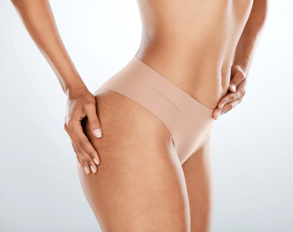A person wearing seamless nude underwear is shown from the side, emphasizing smooth skin and a toned figure, reminiscent of an Evolve Treatment result. The hands rest on the waist and thigh against a plain background.