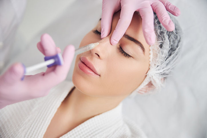 Woman receiving non-surgical nose filler injection from licensed aesthetician