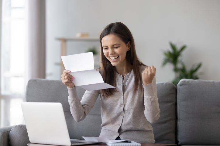 Excited woman opening loan approval letter at home