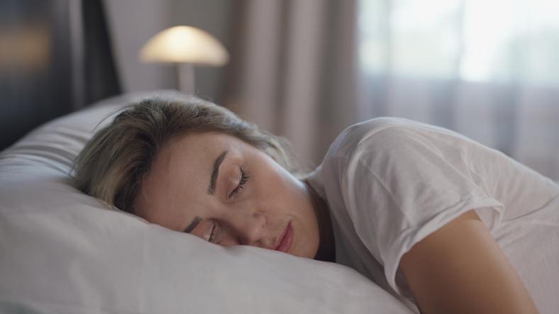 Une femme paisible dort confortablement dans son lit, la tête posée sur un oreiller blanc.