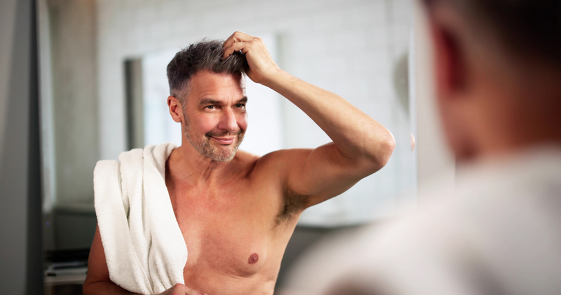 Un homme d'âge mûr sûr de lui vérifie sa coiffure dans le miroir de la salle de bain