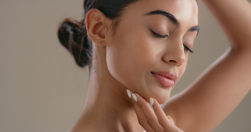 Close-up of a woman with glowing, even-toned skin and eyes closed, gently touching her jawline—illustrating clear, bright results from Q Dermatology care.