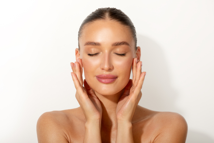 Woman with glowing skin gently touching her face, representing the results of the Vanity Lab membership skincare program.