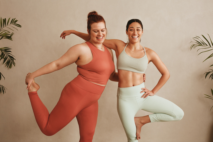 Two women smiling in yoga poses after a workout, showing vitality and balance from learning how to balance hormones
